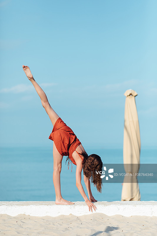 长发少女身穿棕色薄纱连体裤在沙滩上做体操图片素材
