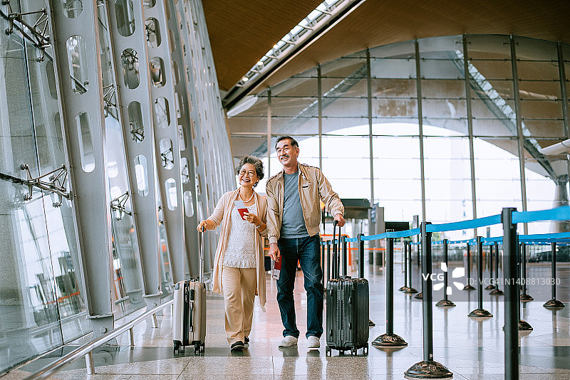 在机场大厅拿着护照和行李的快乐亚洲老年夫妇图片素材