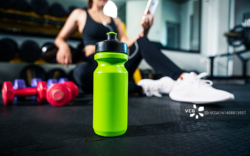 健身房橡胶地板上的矿泉水瓶和哑铃，运动或锻炼概念图片素材