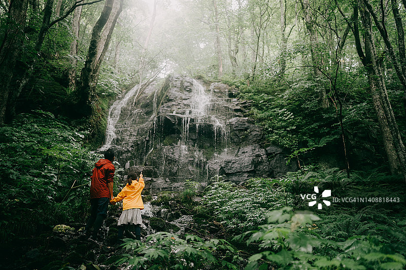 父子在多雨的森林里观看瀑布图片素材