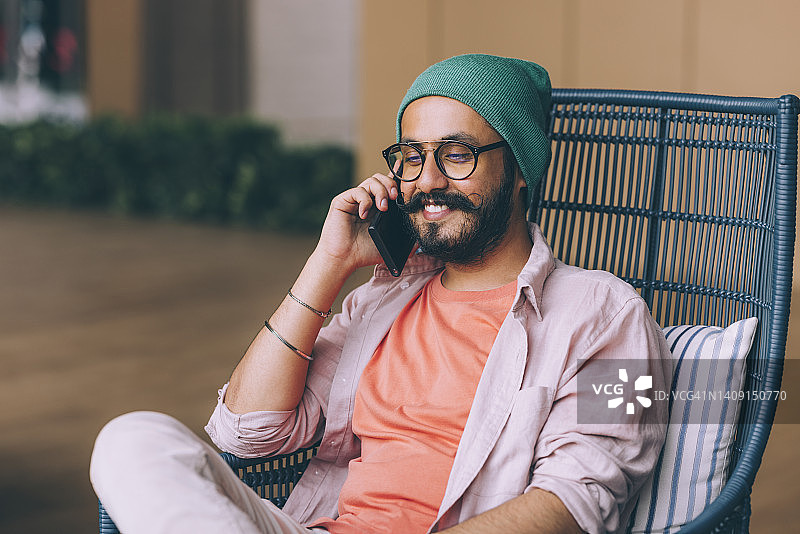 面带微笑，英俊的络腮胡商人坐在户外用手机打电话图片素材
