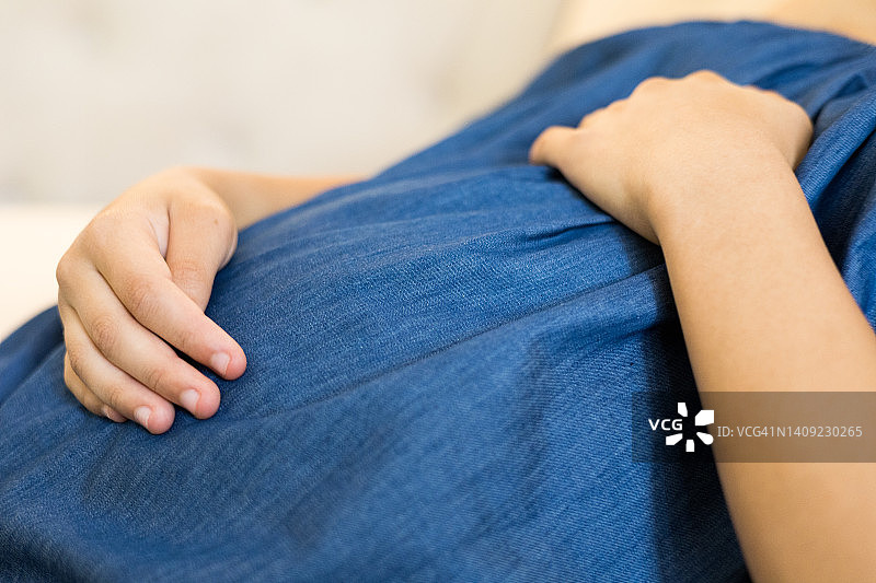 年轻混血孕妇在沙发上休息，抚摸着隆起的肚子图片素材