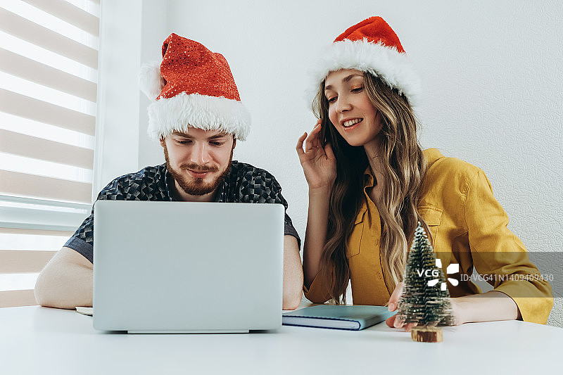 戴着圣诞帽坐在超极本后面的年轻夫妇图片素材