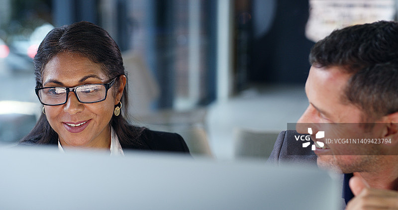 在初创企业中合作的同事们。两个快乐的商务人士在办公室里用电脑工作。一位女同事和一位男同事在公司里工作，微笑地进行合作图片素材