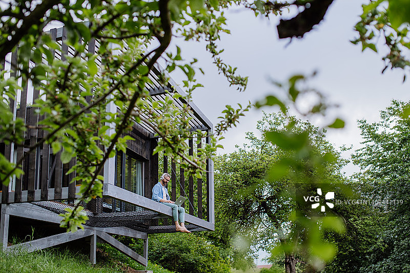 在树屋里用笔记本电脑和耳机工作的男人图片素材