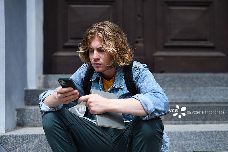 男学生坐在学校楼梯上使用智能手机图片素材