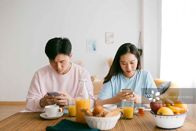 亚洲夫妇早餐时看手机图片素材