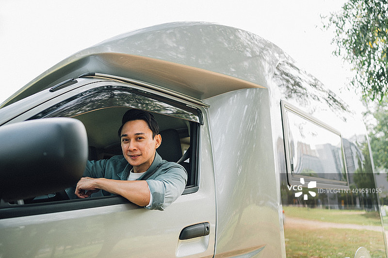 自驾休闲度假：亚洲男人和家人坐在房车驾驶座上，看着窗外微笑图片素材