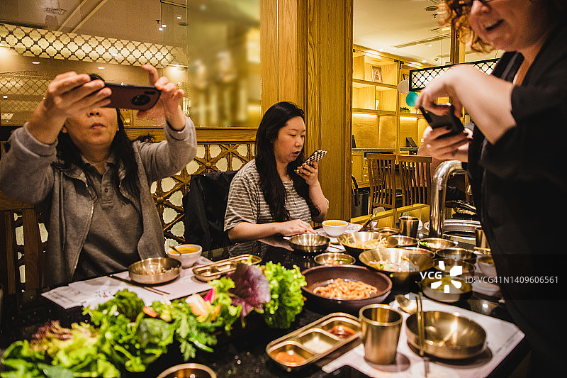朋友在餐厅享用韩国料理并用手机拍照图片素材