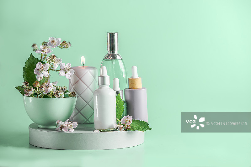 化妆品产品背景，展示台上有各种瓶子、蜡烛、碗、绿叶和鲜花图片素材