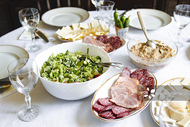 在家中布置的餐桌俯视图，白色瓷碗里盛满绿色沙拉、熟食拼盘、葡萄酒杯和盘子图片素材