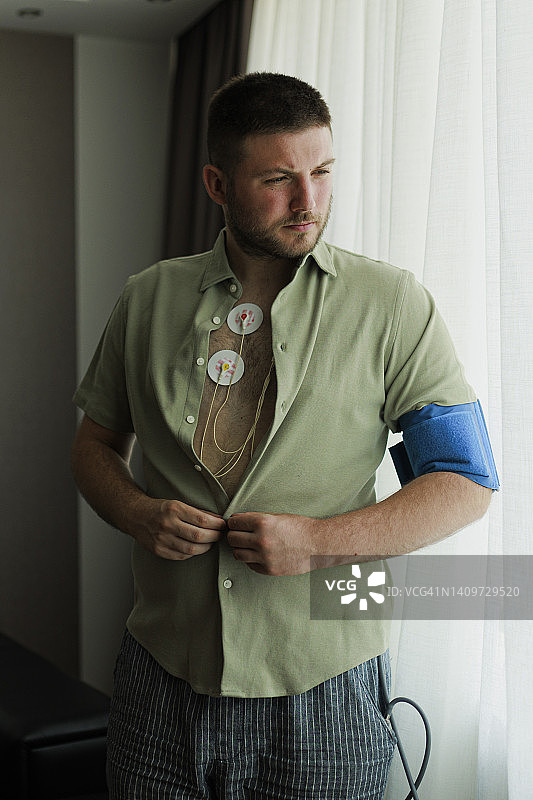 年轻男子佩戴心率监测器穿衣服。心脏工作研究，心脏病学。Holter监测器。医疗诊断。保健，医院。心电图传感器 - 心电图和血压测量图片素材