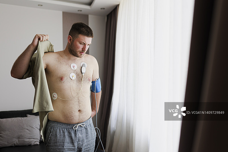 年轻男子佩戴心率监测器穿衣服。心脏工作研究，心脏病学。Holter监测器。医疗诊断。保健，医院。心电图传感器 - 心电图和血压测量图片素材