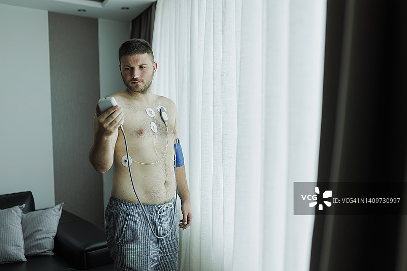 年轻男人使用心率监测器，心脏工作研究，心脏病学，动态心电图监测器，医疗诊断，医疗保健，医院，心电图传感器和血压测量图片素材