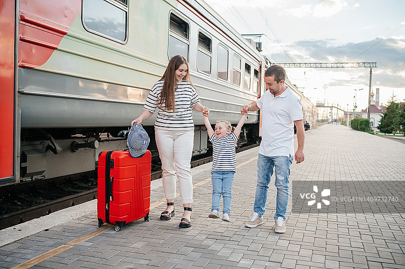 快乐的儿童带着人工耳蜗，在父母的怀里荡秋千，母亲提着红色手提箱图片素材