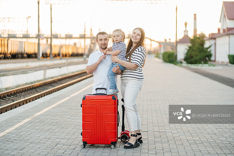 妈妈、爸爸和戴着人工耳蜗的女儿在火车站，带着一个红色大行李箱图片素材