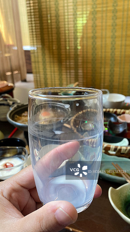 手拿空牛奶杯，背景是日式料理的特写图片素材