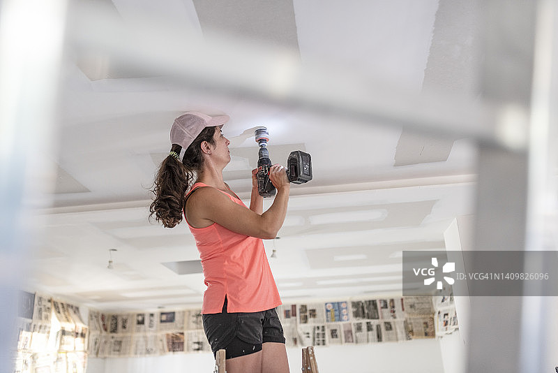 女人用钻头和圆形钻头在石膏板天花板上钻孔，安装舷窗灯图片素材