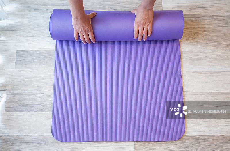 在家锻炼后，女人双手折叠紫色瑜伽垫或健身垫的俯视图图片素材