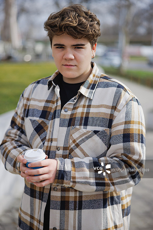穿着伐木工衬衫的少年拿着外卖咖啡，在户外看着镜头图片素材