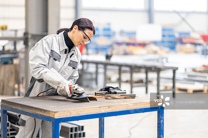 棕发女工用砂轮机研磨金属零件图片素材