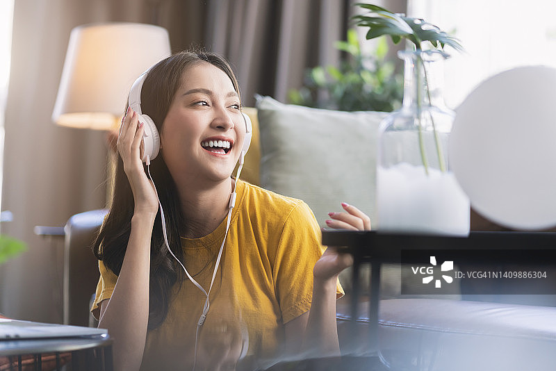 亚裔女子在沙发上听音乐，面带微笑放松身心图片素材