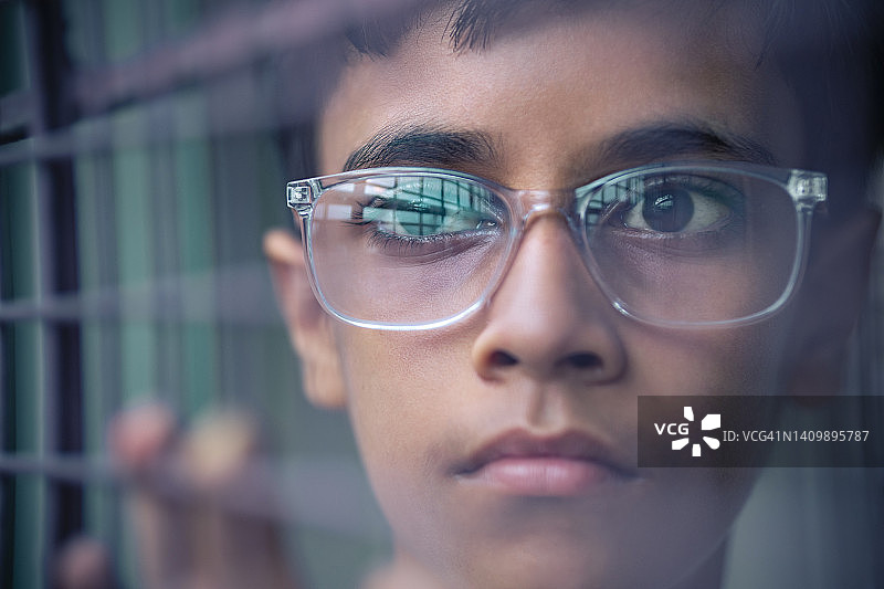 少年站在金属栅栏网后沉思图片素材