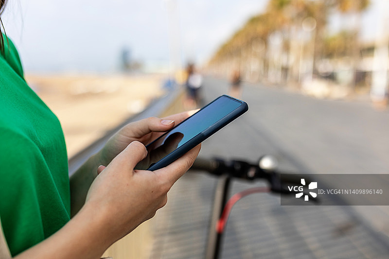 女子户外骑行滑板车时使用智能手机特写图片素材