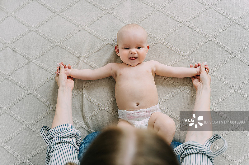 可爱的宝宝躺在家里的浅米色毯子上。妈妈带着宝宝做体操。图片素材