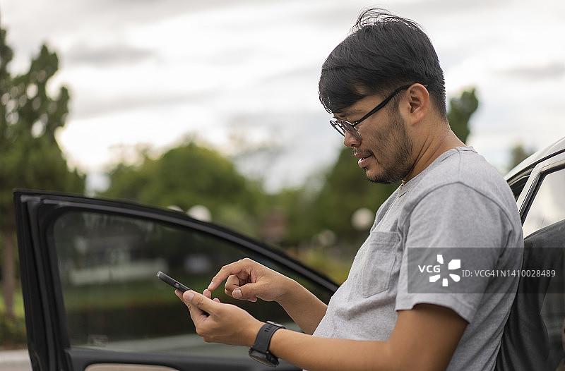 亚洲年轻旅行者靠车用手机图片素材