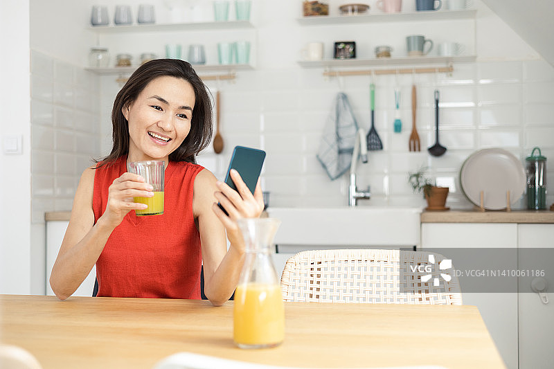 快乐的亚洲女人喝着果汁，进行视频通话图片素材