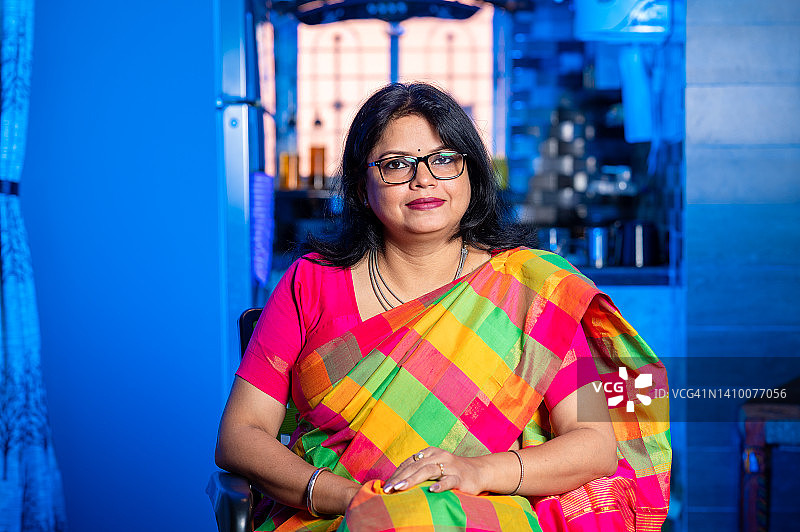 穿着传统纱丽坐在沙发上的印度族快乐女人的肖像图片素材