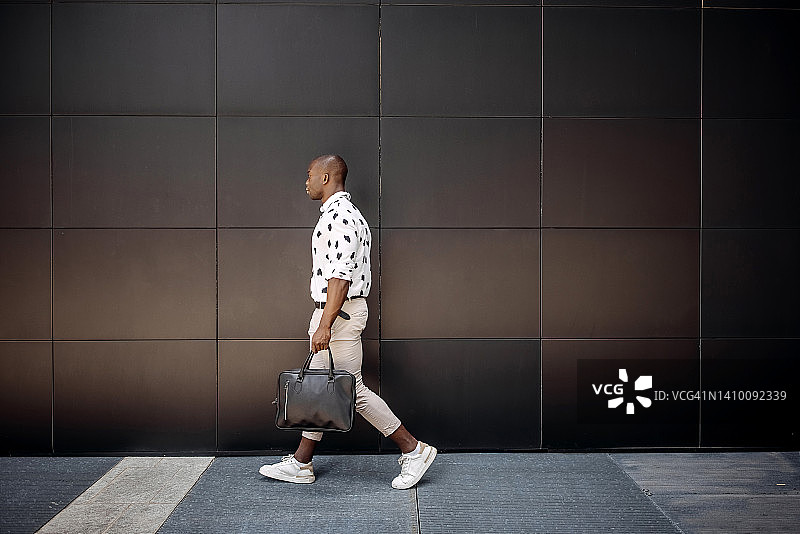 年轻英俊的商人在城市黑色墙壁前行走图片素材