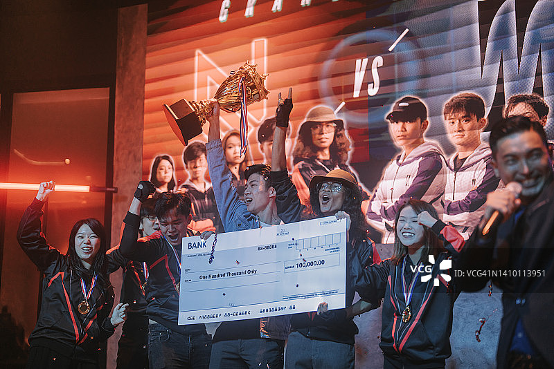 亚洲电竞团队手持奖杯模型支票，在舞台上欢呼雀跃，庆祝赢得视频游戏总决赛。视频游戏锦标赛竞技场。电子游戏锦标赛赛事图片素材