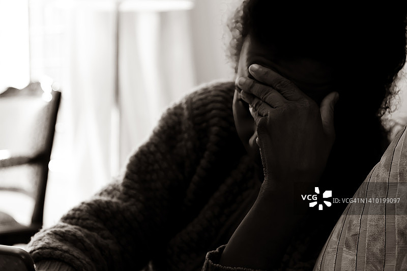 美国的精神抑郁：沮丧的黑人妇女坐在沙发上，手放在头上拿着智能手机图片素材