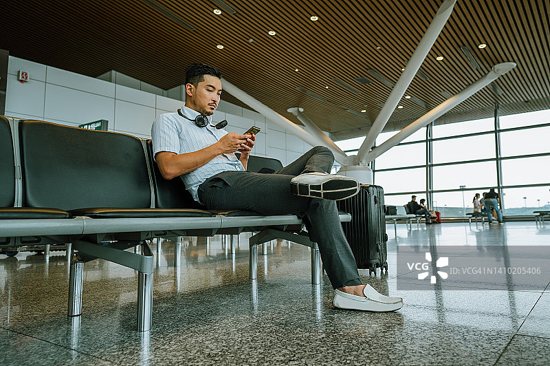 亚裔男子在机场航站楼候机时使用智能手机图片素材