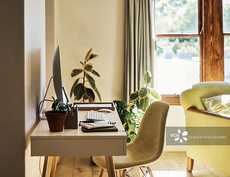 明亮客厅中的居家办公桌，配有台式电脑。 现代工作空间的时尚室内设计装饰，采用时尚的色彩，在温暖舒适的房间内在家工作或从事自由职业图片素材