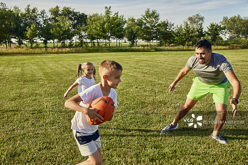 晴天，父亲和儿子女儿在运动场上打橄榄球图片素材