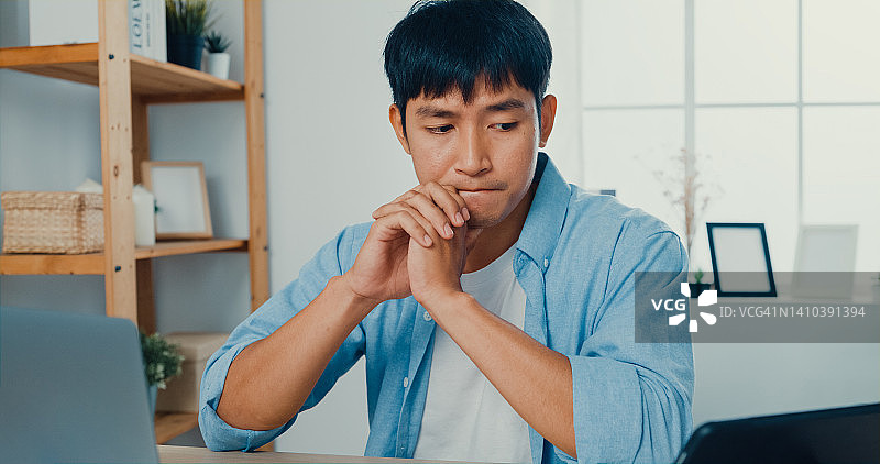 在家中客厅的办公桌旁使用笔记本电脑和平板电脑工作的年轻人图片素材