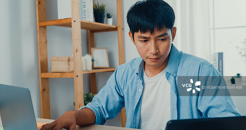 在家中客厅工作桌旁使用笔记本电脑和平板电脑工作的年轻男人特写图片素材