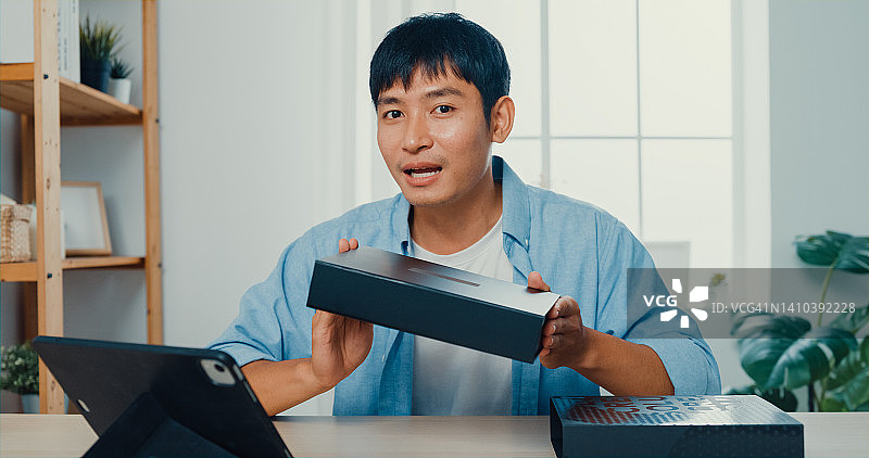 年轻男子在家中客厅的工作桌旁拍摄开箱视频图片素材