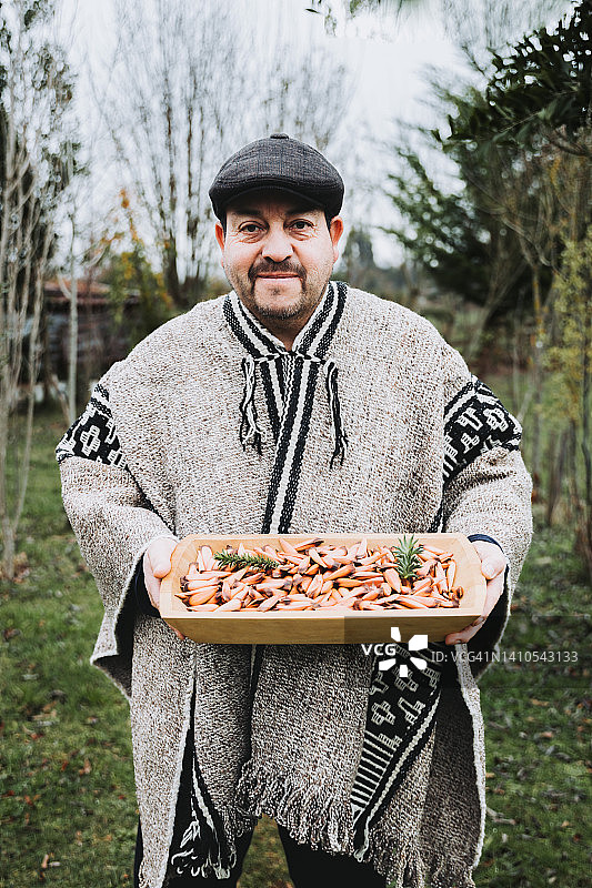 使用羊毛披肩的传统马普切男人，手持装有智利南洋杉松子的简朴木槽图片素材