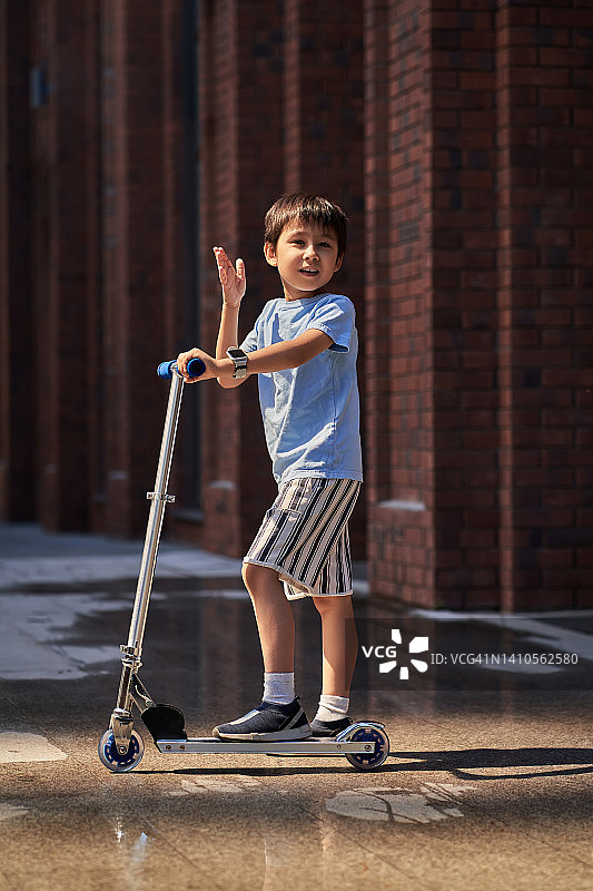 男孩在建筑物附近的街道上骑滑板车图片素材