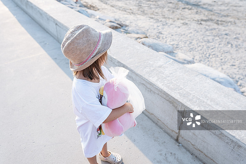 在海滩长廊玩粉色娃娃的小女孩图片素材