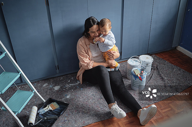 母亲做手工，抱着宝宝，在新家粉刷儿童房。单亲妈妈独自装修公寓时与新生儿子一起休息。搬家后，父母坐在卧室里图片素材