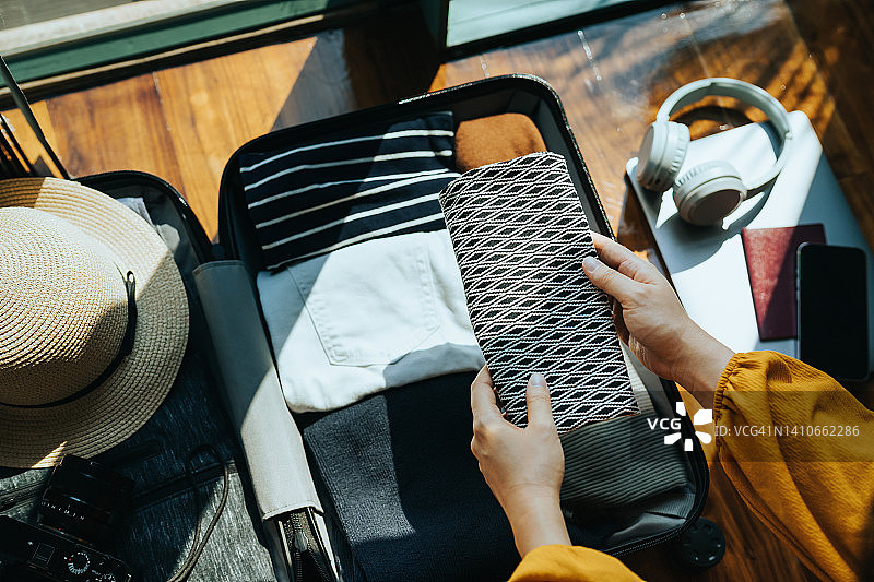 在家打包行李准备旅行的女子，配有太阳帽、相机、衣物、耳机、笔记本电脑、智能手机和护照。旅行概念图片素材