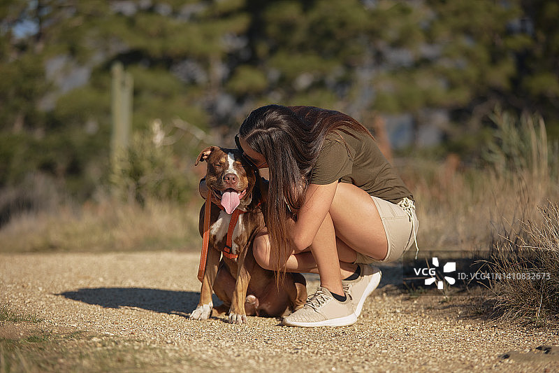 年轻女人表达对情感支持动物的爱意：女人和比特犬的自然漫步图片素材