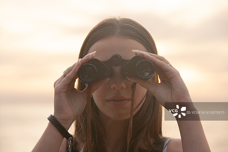 年轻女子用双筒望远镜远眺日落水面图片素材