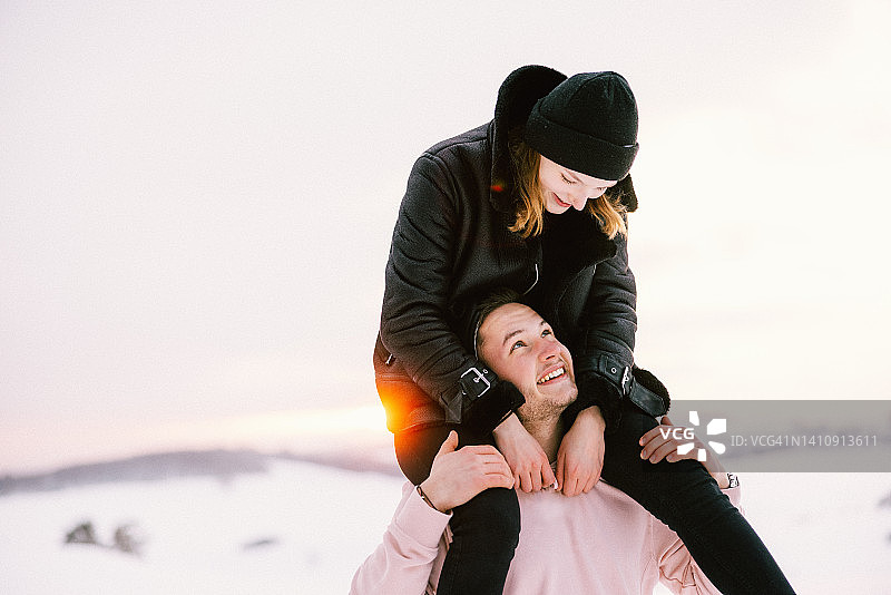 户外冬季风景中，女人背着男人，年轻情侣玩得很开心图片素材