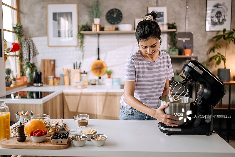 在家庭厨房中使用电动搅拌机的女人图片素材